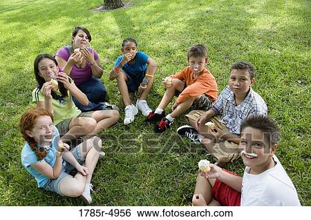 Children and their teacher sitting in a circle on the grass eating cupcakes View Large Photo Image Stock Photograph - Children and their teacher sitting in a circle on the grass eating cupcakes. Fotosearch