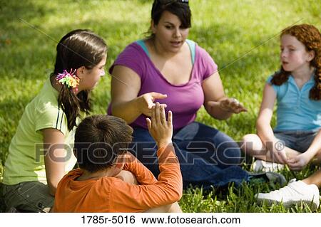 Children and their teacher sitting in a circle on the grass at a park View Large Photo Image Stock Photograph - Children and their teacher sitting in a circle on the grass at a park. Fotosearch