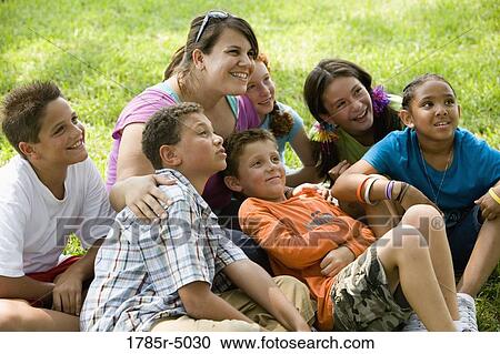 Children and their teacher sitting on the grass at a park watching View Large Photo Image Stock Image - Children and their teacher sitting on the grass at a park watching. Fotosearch