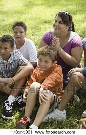 Children and their teacher sitting on the grass at a park watching View Large Photo Image Stock Image - Children and their teacher sitting on the grass at a park watching. Fotosearch