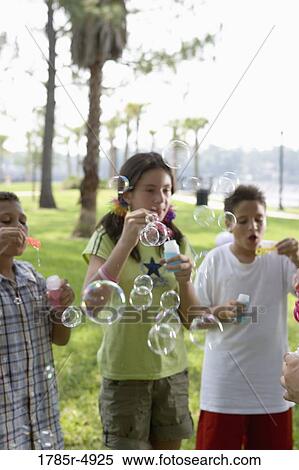 Children blowing bubbles at a park View Large Photo Image Stock Photography - Children blowing bubbles at a park. Fotosearch