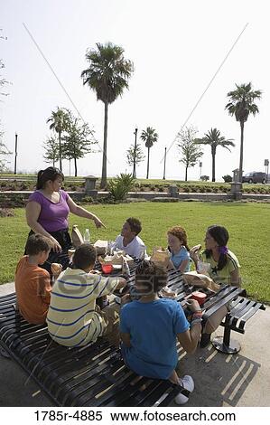 Children sitting at picnic table having refreshments with their teacher in a park View Large Photo Image Stock Photography - Children sitting at picnic table having refreshments with their teacher in a park. Fotosearch