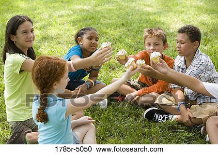 Children sitting in a circle on grass cheering over cupcakes View Large Photo Image Stock Image - Children sitting in a circle on grass cheering over cupcakes. Fotosearch