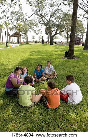 Children sitting in a circle on the grass with their teacher at a park View Large Photo Image Picture - Children sitting in a circle on the grass with their teacher at a park. Fotosearch