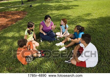 Children sitting in a circle on the grass with their teacher at a park View Large Photo Image Stock Image - Children sitting in a circle on the grass with their teacher at a park. Fotosearch