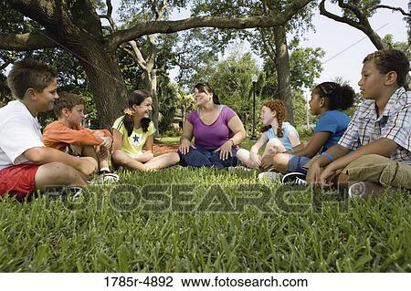 Children sitting in a circle on the grass with their teacher at a park View Large Photo Image Stock Image - Children sitting in a circle on the grass with their teacher at a park. Fotosearch