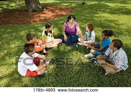 Children sitting in a circle on the grass with their teacher at a park View Large Photo Image Stock Image - Children sitting in a circle on the grass with their teacher at a park. Fotosearch