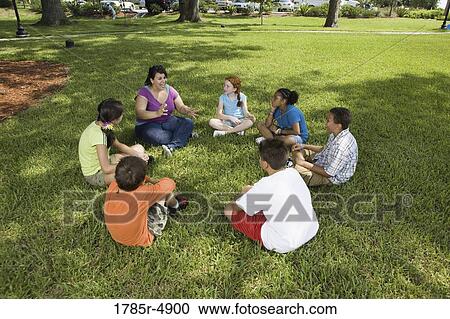 Children sitting in a circle on the grass with their teacher at a park View Large Photo Image Stock Image - Children sitting in a circle on the grass with their teacher at a park. Fotosearch