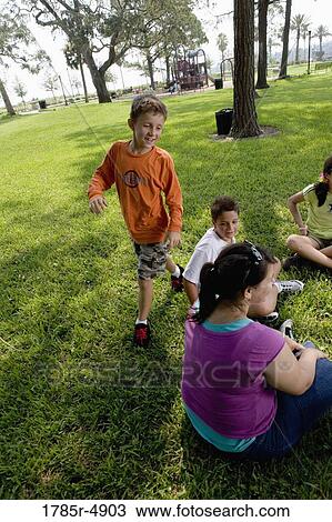 Children sitting in a circle on the grass with their teacher while a boy walks around them View Large Photo Image Stock Image - Children sitting in a circle on the grass with their teacher while a boy walks around them. Fotosearch
