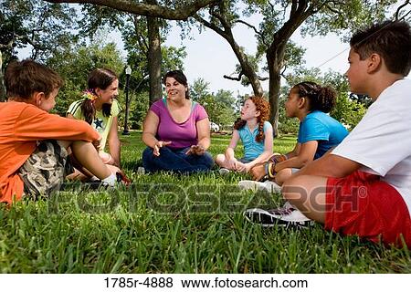 Children sitting in a circle on the grass with their teacher at a park View Large Photo Image Stock Photo - Children sitting in a circle on the grass with their teacher at a park. Fotosearch