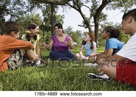 Children sitting in a circle on the grass with their teacher at a park View Large Photo Image Stock Photo - Children sitting in a circle on the grass with their teacher at a park. Fotosearch