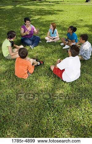 Children sitting in a circle on the grass with their teacher at a park View Large Photo Image Stock Photo - Children sitting in a circle on the grass with their teacher at a park. Fotosearch
