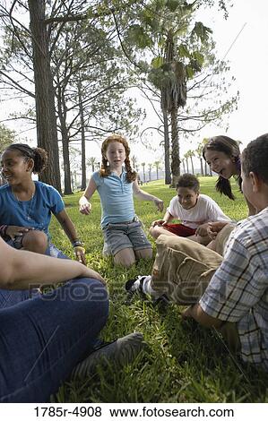 Stock Photo - Children sitting in a circle on the grass with their teacher at a park. Fotosearch
