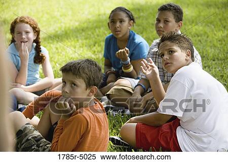 Stock Photography - Children sitting in a circle on the grass at a park. Fotosearch