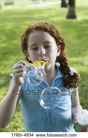 Picture - Close-up of a girl blowing bubbles at a park. Fotosearch
