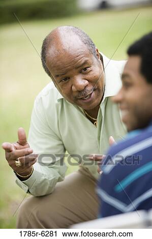 Stock Image - Close-up of a mature man talking to adult son. Fotosearch