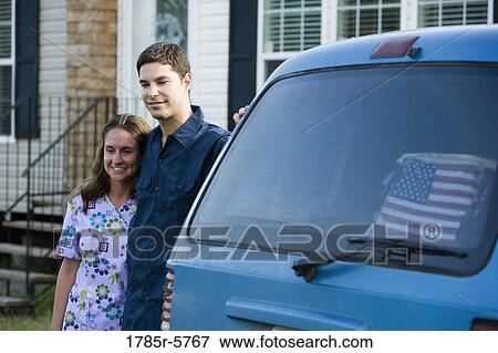 Close-up of a young couple standing by a car in front of a house View Large Photo Image Stock Photo - Close-up of a young couple standing by a car in front of a house. Fotosearch