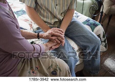Stock Image - Close-up of elderly mother holding son's hands. Fotosearch