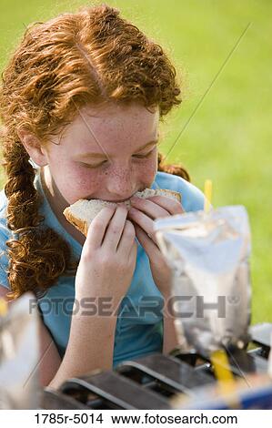 Close-up of girl biting into a sandwich at a picnic table View Large Photo Image Picture - Close-up of girl biting into a sandwich at a picnic table. Fotosearch