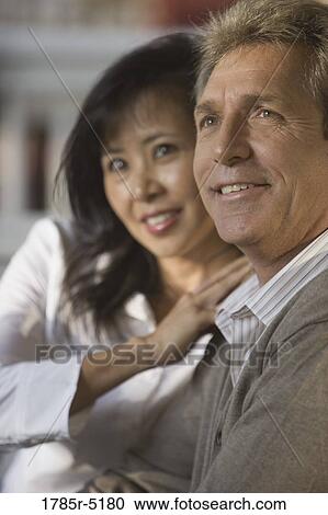 Stock Image - Close up of mature interracial couple sitting on front porch. Fotosearch