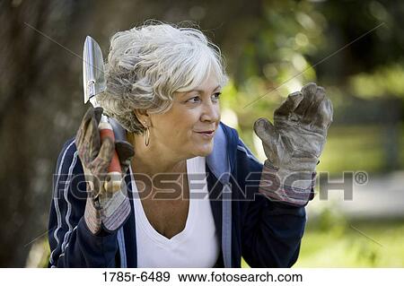 Stock Photo - Close-up of mature woman wearing work gloves and holding a gardening tool. Fotosearch