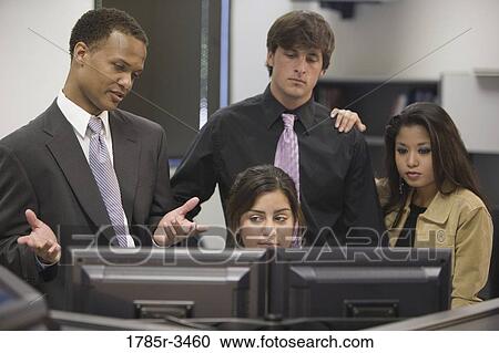 Stock Image - Close-up of office workers gathered around computer. Fotosearch
