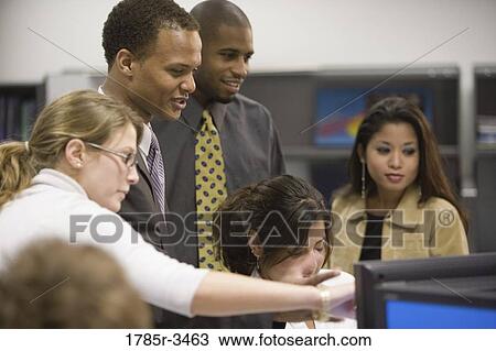 Stock Image - Close-up of office workers gathered around computer. Fotosearch