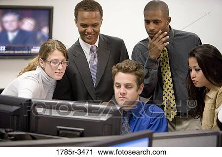 Stock Image - Close-up of office workers gathered around computer. Fotosearch