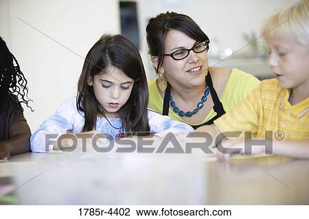 Close up of teacher helping young children in class View Large Photo Image Stock Image - Close up of teacher helping young children in class. Fotosearch