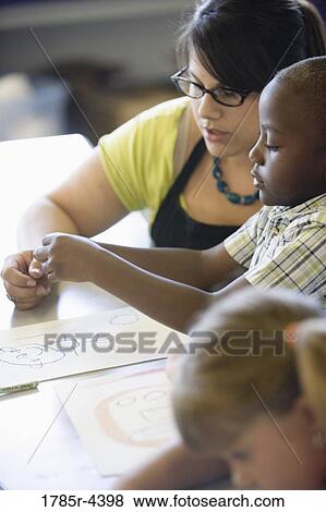 Close up of teacher helping young children in class View Large Photo Image Stock Photo - Close up of teacher helping young children in class. Fotosearch