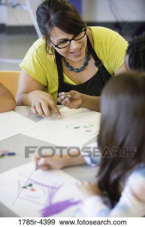 Stock Photo - Close up of teacher helping young children in class. Fotosearch