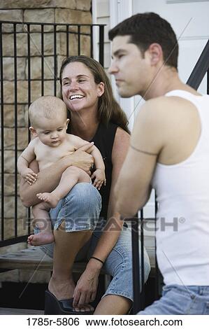 Stock Photograph - Close up of young parents with baby on front steps of house. Fotosearch