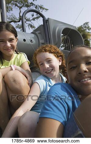 Close-up view of laughing children sitting on a slide at a playground View Large Photo Image Stock Photo - Close-up view of laughing children sitting on a slide at a playground. Fotosearch