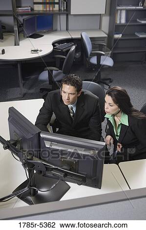 Stock Image - Co-workers working together at a desk looking at computer screens. Fotosearch