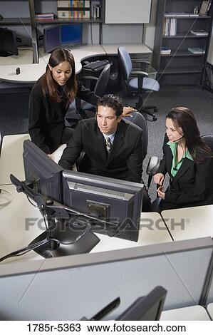 Co-workers working together at a desk looking at computer screens View Large Photo Image Stock Image - Co-workers working together at a desk looking at computer screens. Fotosearch