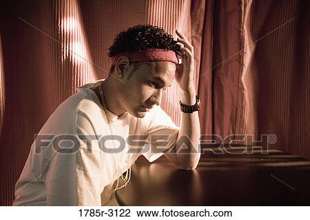 Contemplative young man in hip-hop fashion sitting at a table View Large Photo Image Stock Image - Contemplative young man in hip-hop fashion sitting at a table. Fotosearch
