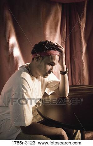 Contemplative young man in hip-hop fashion sitting at a table View Large Photo Image Stock Image - Contemplative young man in hip-hop fashion sitting at a table. Fotosearch