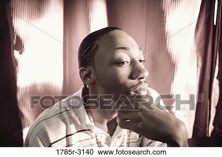 Stock Image - Contemplative young man in hip-hop fashion sitting at a table. Fotosearch