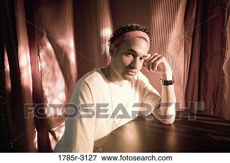 Contemplative young man in hip-hop fashion sitting at a table View Large Photo Image Stock Photo - Contemplative young man in hip-hop fashion sitting at a table. Fotosearch