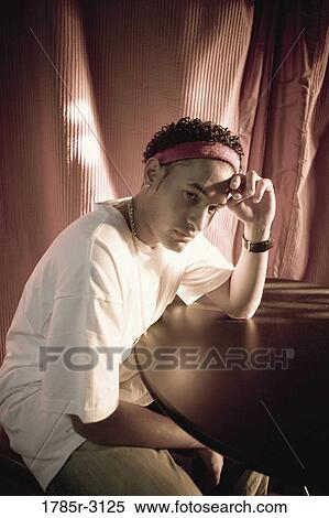 Contemplative young man in hip-hop fashion sitting at a table View Large Photo Image Stock Photography - Contemplative young man in hip-hop fashion sitting at a table. Fotosearch