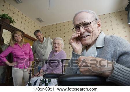Stock Image - Elderly man whispering to camera with spouse and adult children in background. Fotosearch