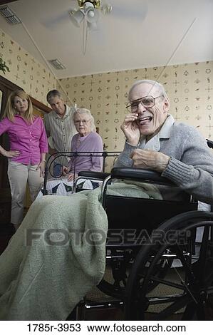 Stock Image - Elderly man whispering to camera with spouse and adult children in background. Fotosearch