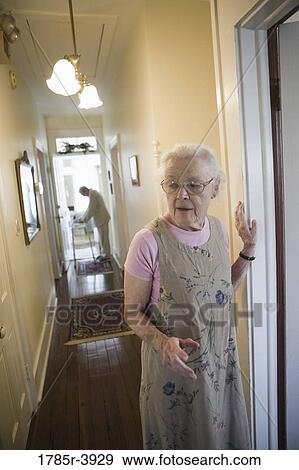 Elderly woman standing in hallway with feeble senior man in the background View Large Photo Image Stock Photo - Elderly woman standing in hallway with feeble senior man in the background. Fotosearch