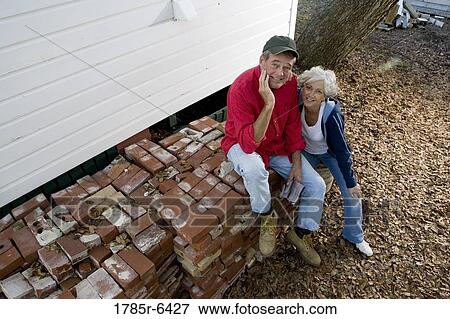 Elevated view of mature couple sitting on stack of bricks outside house View Large Photo Image Stock Photo - Elevated view of mature couple sitting on stack of bricks outside house. Fotosearch