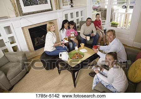 Stock Image - Family and friends having breakfast together in living room. Fotosearch