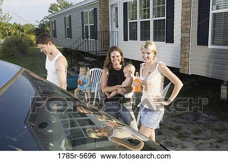 Stock Photograph - Family and friends standing next to car outside trailer home. Fotosearch