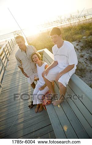 Picture - Family sitting on wooden pier at beach at sunrise. Fotosearch