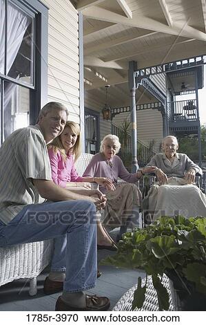 Stock Image - Family with elderly parents and adult children sitting together on front porch. Fotosearch