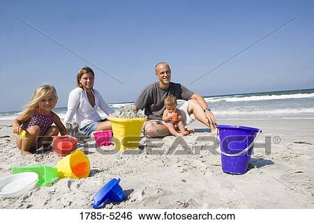 Family with two young girls sitting on beach playing with buckets and shovels View Large Photo Image Stock Photograph - Family with two young girls sitting on beach playing with buckets and shovels. Fotosearch