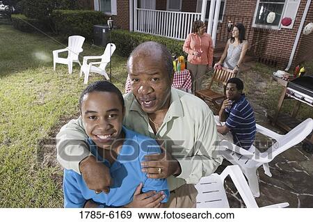 Father and son enjoying backyard bbq with family in background View Large Photo Image Stock Photo - Father and son enjoying backyard bbq with family in background. Fotosearch